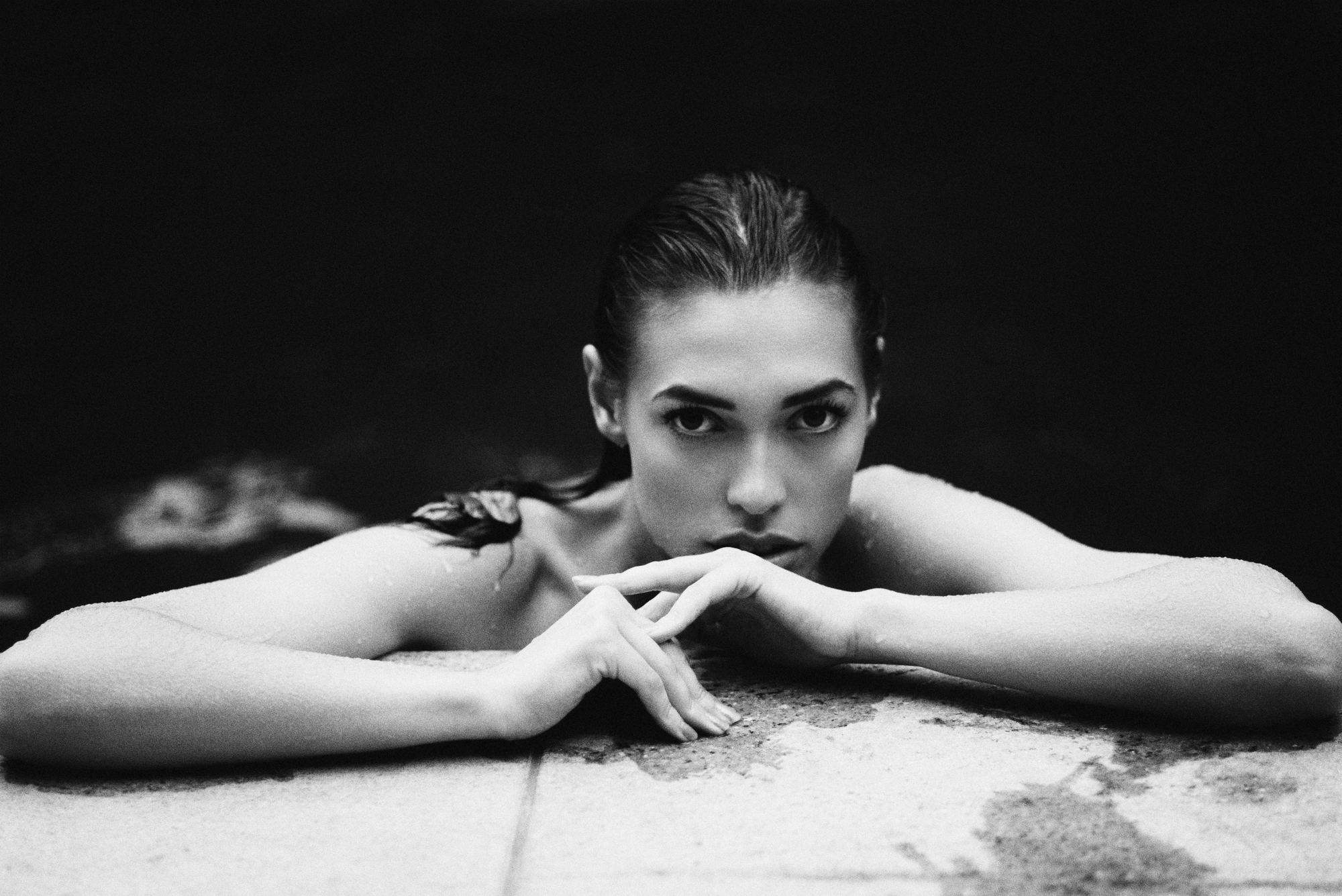 Editorial portrait of a woman resting her chin on her hands on wet stone, black and white, by Armand Sanchez